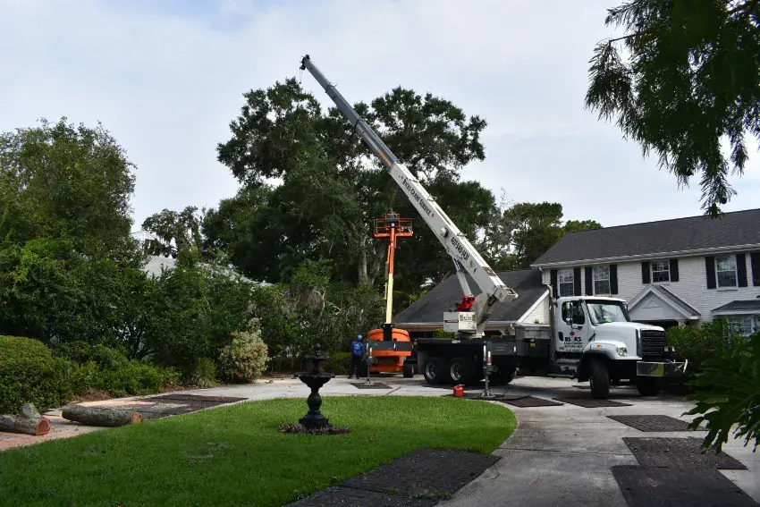 Bucket truck and crane staged on ground protection mats in a residential driveway