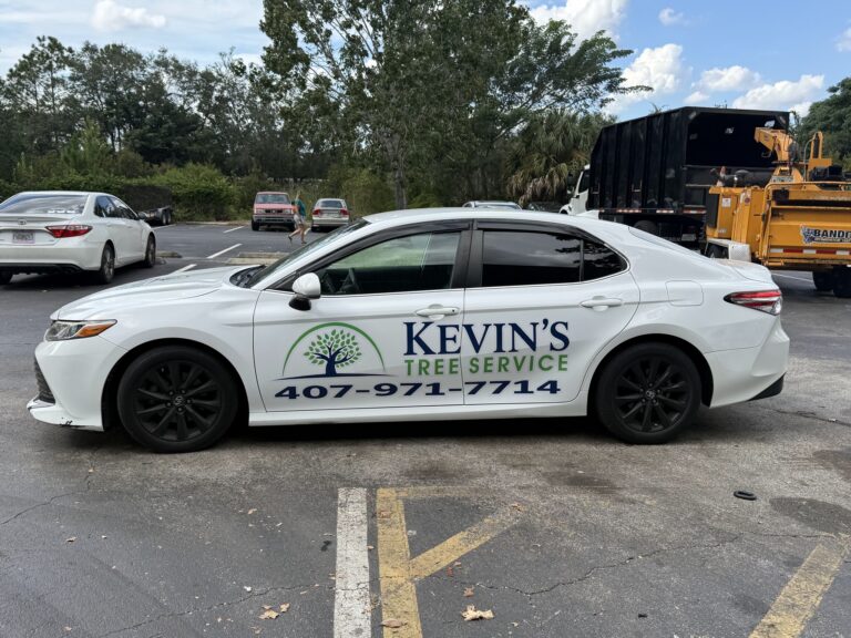 White Toyota Camry wrapped with the Kevin's Tree Service logo and phone number 407-971-7714, parked with a chip truck and chipper behind it