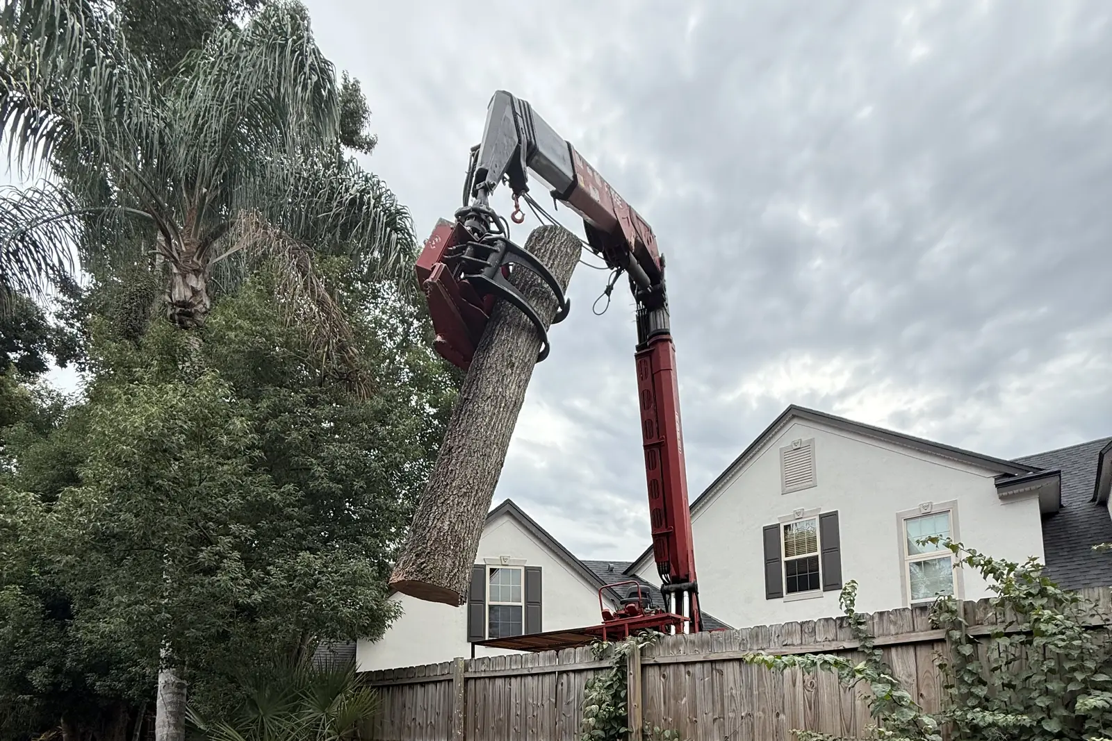 Grapple crane lifting a cut trunk section over a backyard fence during a tree removal in Central Florida