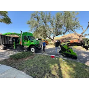 Compact track loader working beside a grapple truck at a residential job